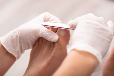Close-up Of Beautician Hand Filling Man's Toe Nail In Salon