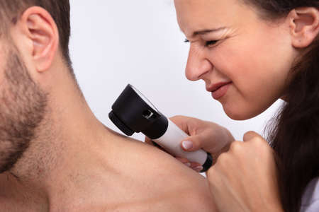 Close-up Of A Young Female Doctor Checking Skin On Man's Neck With Dermatoscope