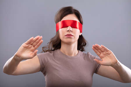 Young Woman's Eye Covered With Red Ribbon On Grey Backgroundの写真素材
