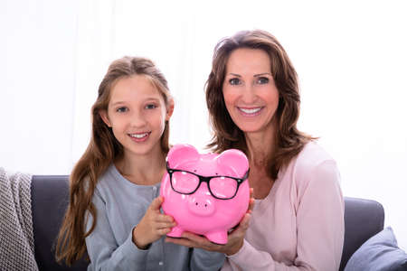 Portrait Of Smiling Mother And Daughter Holding Pink Piggybankの写真素材