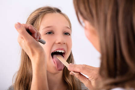 Close-up Of Doctor Checking Girl's Sore Throat With Tongue Depressor