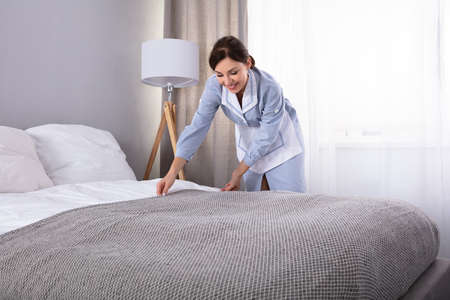 Smiling Female Housekeeper Making Bed In Hotel Roomの写真素材