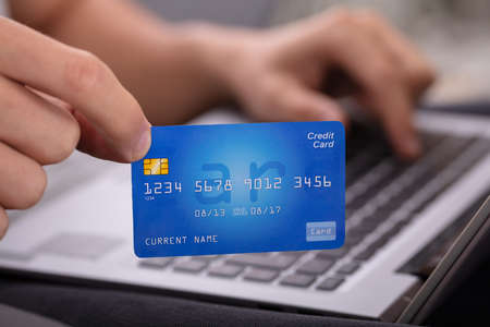 Close-up Of A Man's Hand Holding Credit Card While Shopping Online On Laptopの写真素材