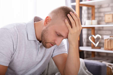 Side View Of A Upset Young Man Sitting On Sofa