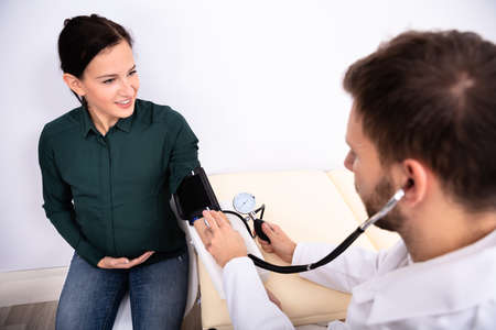 Young Male Doctor Checking Blood Pressure Of Smiling Female Patient In Clinicの写真素材