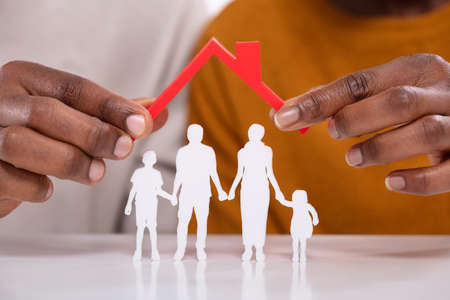 Close-up Of A Person's Hand Protecting Family Figures With Red Roof