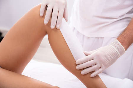 Male Beautician Hand Waxing Woman's Leg With Wax Strip