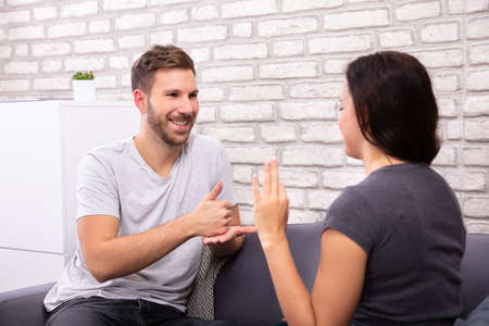 Smiling Young Couple Sitting On Sofa Communicating With Sign Language