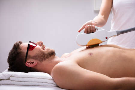 Young Female Beautician Giving Laser Depilation Treatment On Relaxed Man's Chest