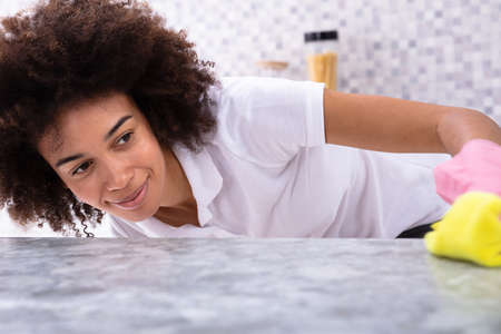 Happy African Young Woman Cleaning Dirty Kitchen Counter With Spray Detergent And Yellow Napkin