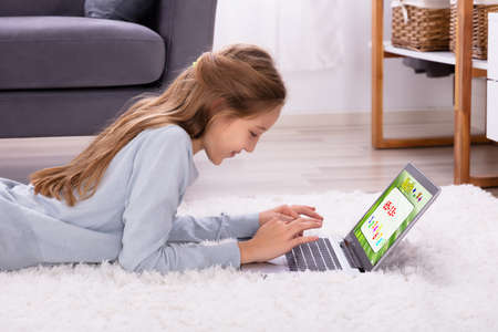 Girl Lying On Carpet Solving Math On Laptop At Home