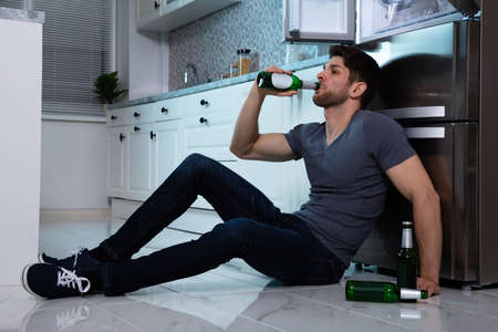Side View Of Young Man Drinking Beer In Front Of Refrigeratorの写真素材