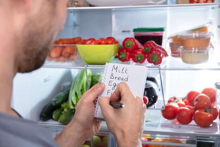 Young Man Writing Shopping List Near Open Refrigeratorの写真素材