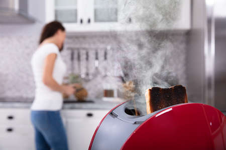 Close-up Of A Red Toaster With Burnt Toast While Woman Working In Kitchenの写真素材