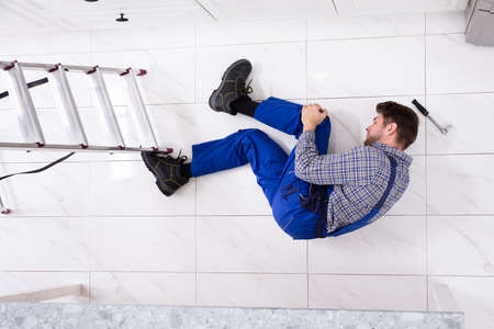 High Angle View Of Injured Worker Lying On Floor Near Ladderの写真素材