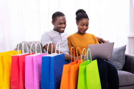 Smiling Young Couple Shopping On Laptop Near Colorful Shopping Bagsの写真素材
