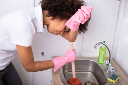 Tired Person Wearing Pink Gloves Cleaning Sink Filled With Water With Cup Plungerの写真素材