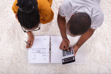 Young African Couple Lying On Carpet Invoice With Calculatorの写真素材