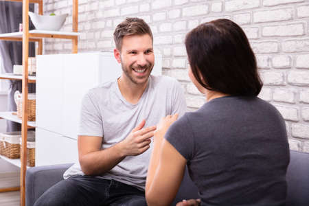 Smiling Young Couple Sitting On Sofa Communicating With Sign Language