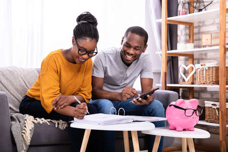 Young African Couple Sitting On Sofa Calculating Invoiceの写真素材