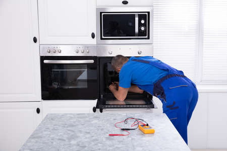 Mature Technician In Overall Repairing Oven In Kitchenの写真素材