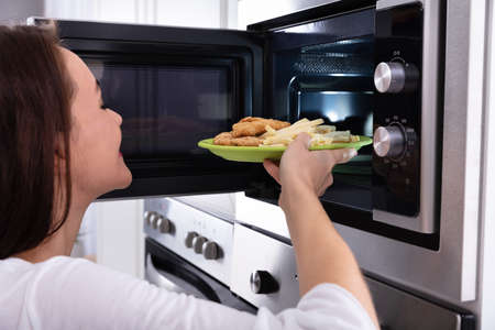 Close-up Of A Young Woman Heating Fried Food In Microwave Ovenの写真素材