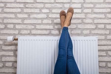 Close-up Of A Woman Warming Up Her Feet On White Radiator At Homeの写真素材