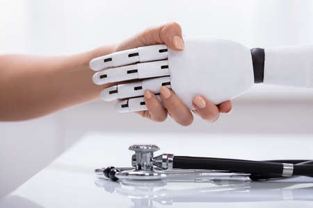 Close-up Of Female Shaking Hand With Robot Over The White Desk With Stethoscopeの写真素材