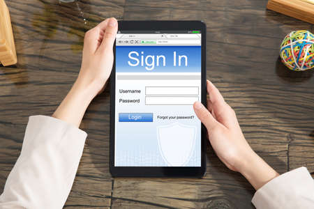 Close-up Of Woman Signing Into Website On Digital Tablet Over Desk