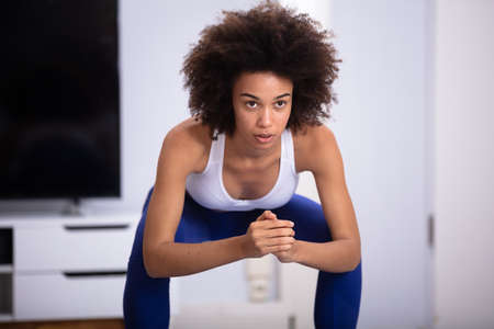 Young Woman In Fitness Wear Doing Squat Exercise At Home