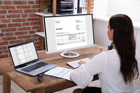 Young Businesswoman Looking At Invoice On Computer Screen In The Office