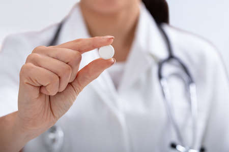 Close-up Of Female Doctor With Stethoscope Around Her Neck Holding White Tablet In Handの写真素材