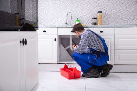 Male Plumber Besides Red Toolbox Fixing Sink In Kitchenの写真素材