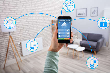 Woman's Hand Using Home Control System On Cellphone With Various Icons