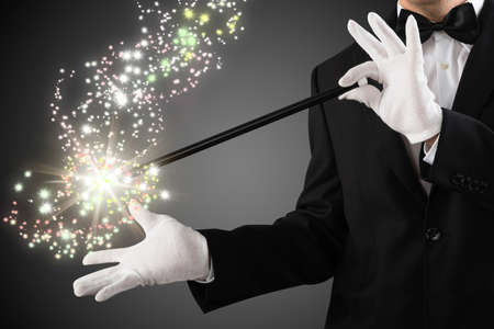 Close-up Of A Magician's Hand Creating Sparkles With Magic Wand On Grey Backgroundの写真素材