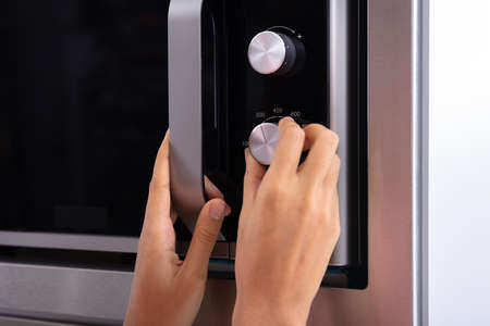 Close-up Of A Smiling Young Woman Adjusting Temperature Of Microwave Ovenの写真素材