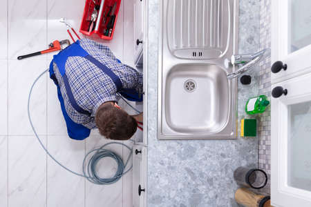 Young Male Plumber Cleaning Clogged Sink Pipe In Kitchenの写真素材