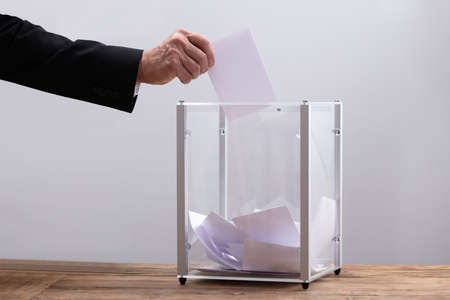 Close-up Of Businessman's Hand Inserting Ballot In A Glass Box