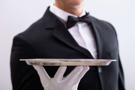 Close-up Of Waiter's Hand Holding Empty Silver Tray Against White Background