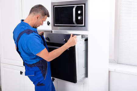 Male Technician Wearing Overall Installing Oven In Kitchenの写真素材