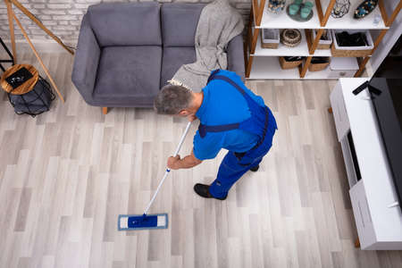 Mature Male Janitor Cleaning Floor With Mop At Home