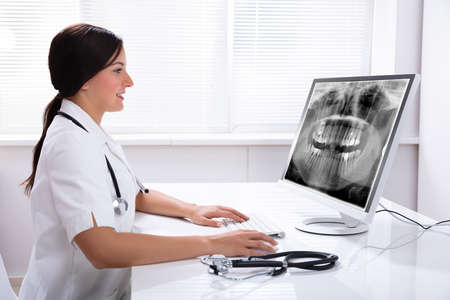 Female Doctor Looking At Teeth X-ray On Computer Over Desk In Clinic