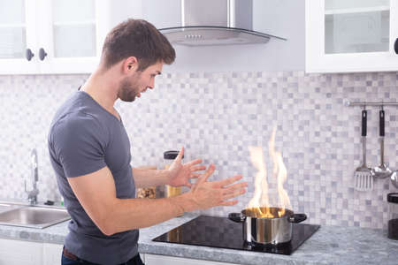 Shocked Young Man Looking At Cooking Pot Burning With Fire On Induction Stoveの写真素材