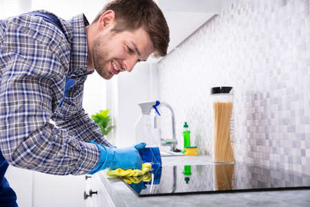Young Happy Man Cleaning Induction Stove With Napkin In Kitchen
