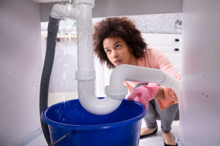 Portrait Of An Young African Woman Looking At Water Leaking From Sink Pipeの写真素材