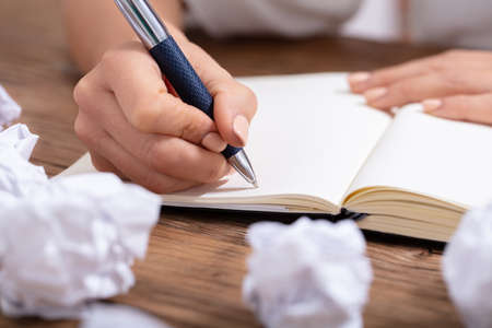 Close-up Of A Person Writing On Blank Notebook With Pen On Wooden Desk