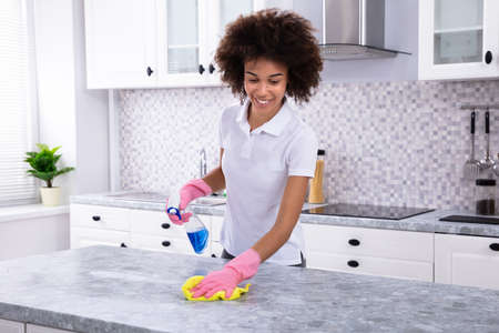 Close-up Of A Young Woman Cleaning Dirty Kitchen Counter With Spray Bottle And Napkinの写真素材