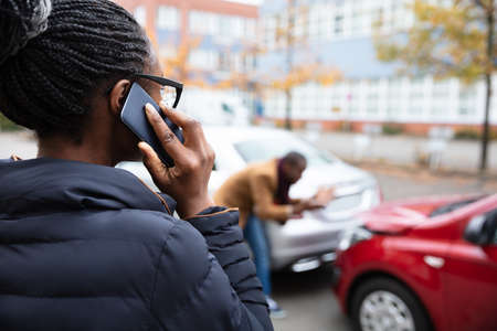 Woman Calling For Assistance In Front Of Man Inspecting Damaged Car On Roadの写真素材