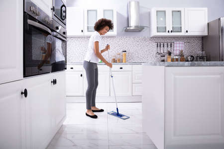 Side View Of A Smiling Female Janitor Cleaning White Floor With Mop In The Kitchenの写真素材