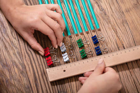 Person Arranging The Colorful Bulldog Clips With Scale On Wooden Desk